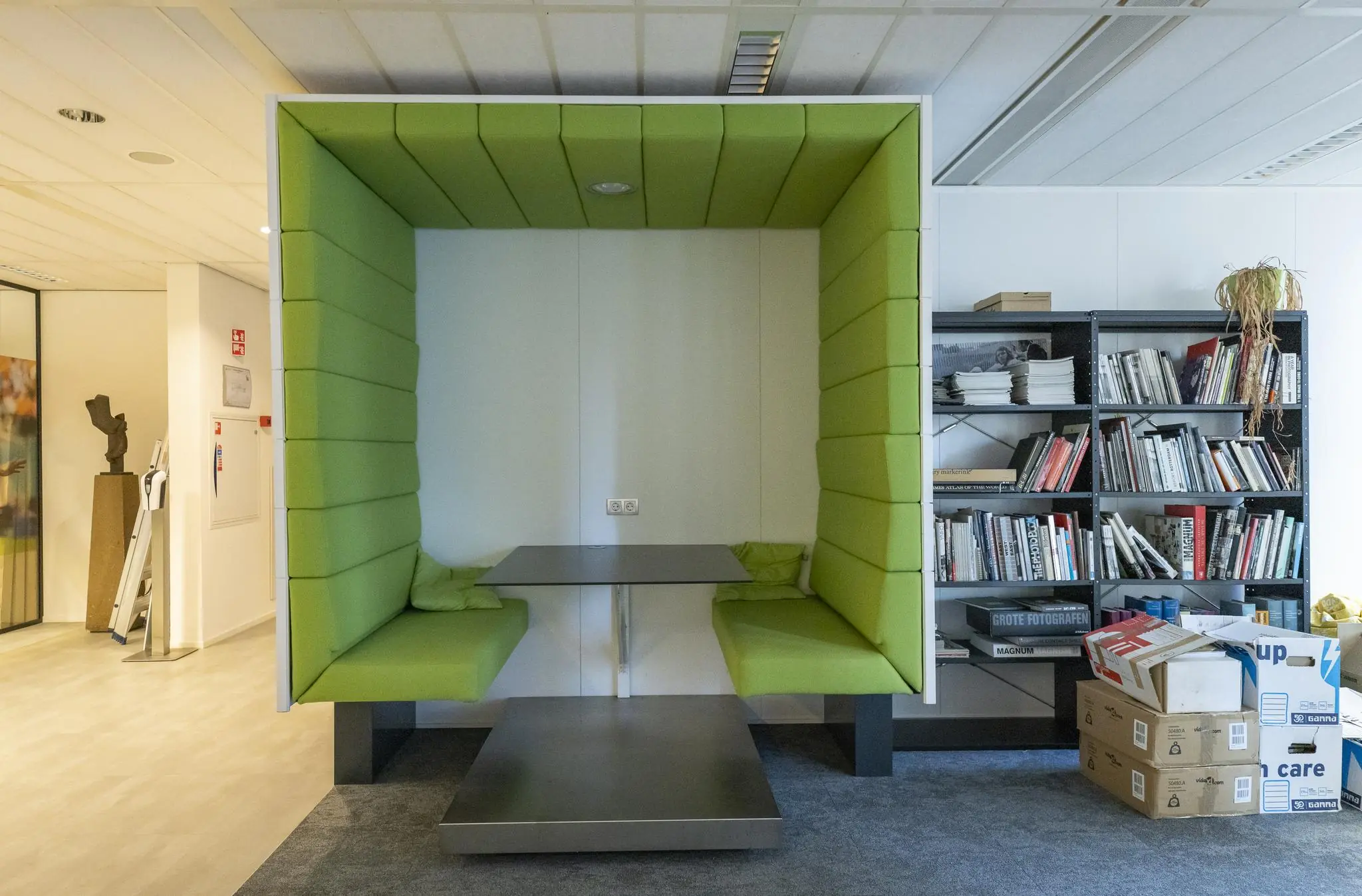 Groene akoestische zitnis met tafel in een modern kantoor aan de Prinses Beatrixlaan, naast een boekenkast en stapels dozen.